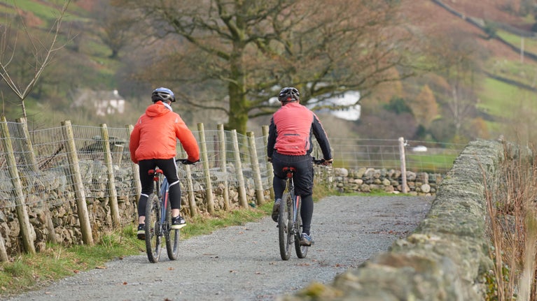 Two cyclists ride along a country track in the Lake District in autumn